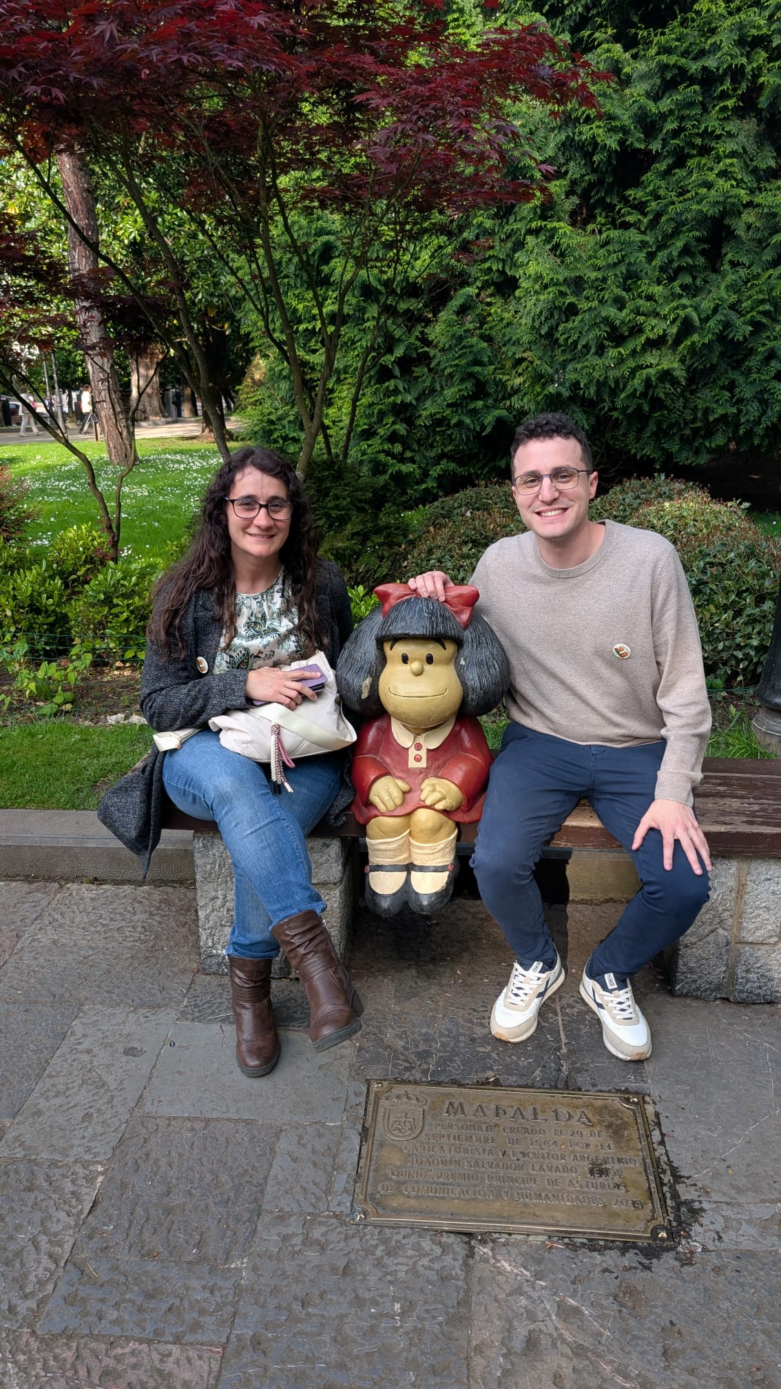 Two nosDeu team members sitting beside the Mafalda statue in Oviedo, illustrating the human side of data and community.